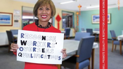 Image of a smiling migrant woman working in aged care holding a sign that reads 'Recognise Workers' Overseas Qualifications'