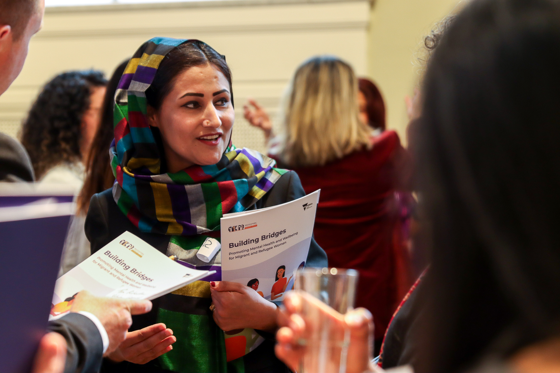 A woman wearing a colourful headscarf holds an MCWH report called Building Bridges