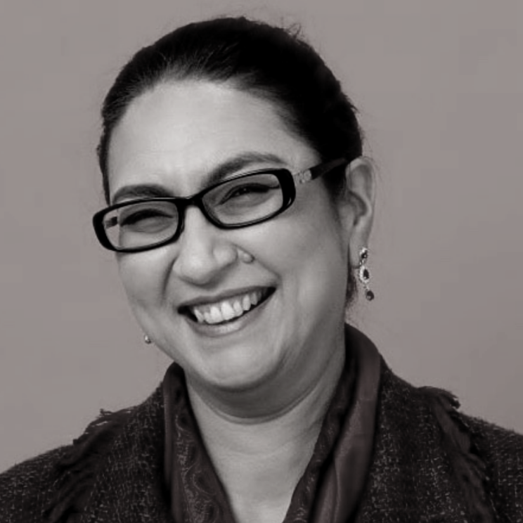 Black and whote headshot of Nisha. She has brown hair tied back, glasses and a smiling expression.