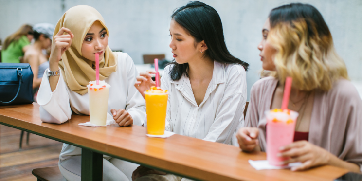 Three women of different ethnicities sitting together having an in depth conversation while drinking milkshakes