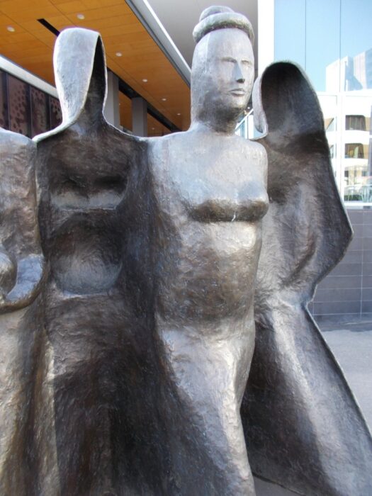 This photograph was taken by me when I was passing the Royal Women's Hospital for my meeting at the Red Cross. I was thinking: "Your mind games, slurs, put-downs and insults made me a shell of a person. I was broken into two pieces- one which 'you think I am' and the other which I think "I am". I doubted my existence, questioned my worth and wondered my place in this world. Then one day I asked myself, "who am I?" Out of the two shells emerged a strong, powerful and elegant woman. That is what I am". We see part of a bronze outdoor statue, that appears to be outside a tall modern building. We can see three or four figures sculpted in bronze, but only one is facing the viewer. The figure is abstract, but clearly striding forward. On either side of this figure, similar figures seem to stride in the opposite direction and we can see the inside imprint of the bronze cast, as if the figures were only shells or moulds.